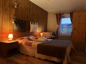 Une pièce comprenant un lit, deux tables de chevet, une fenêtre avec des rideaux et des murs en bois.