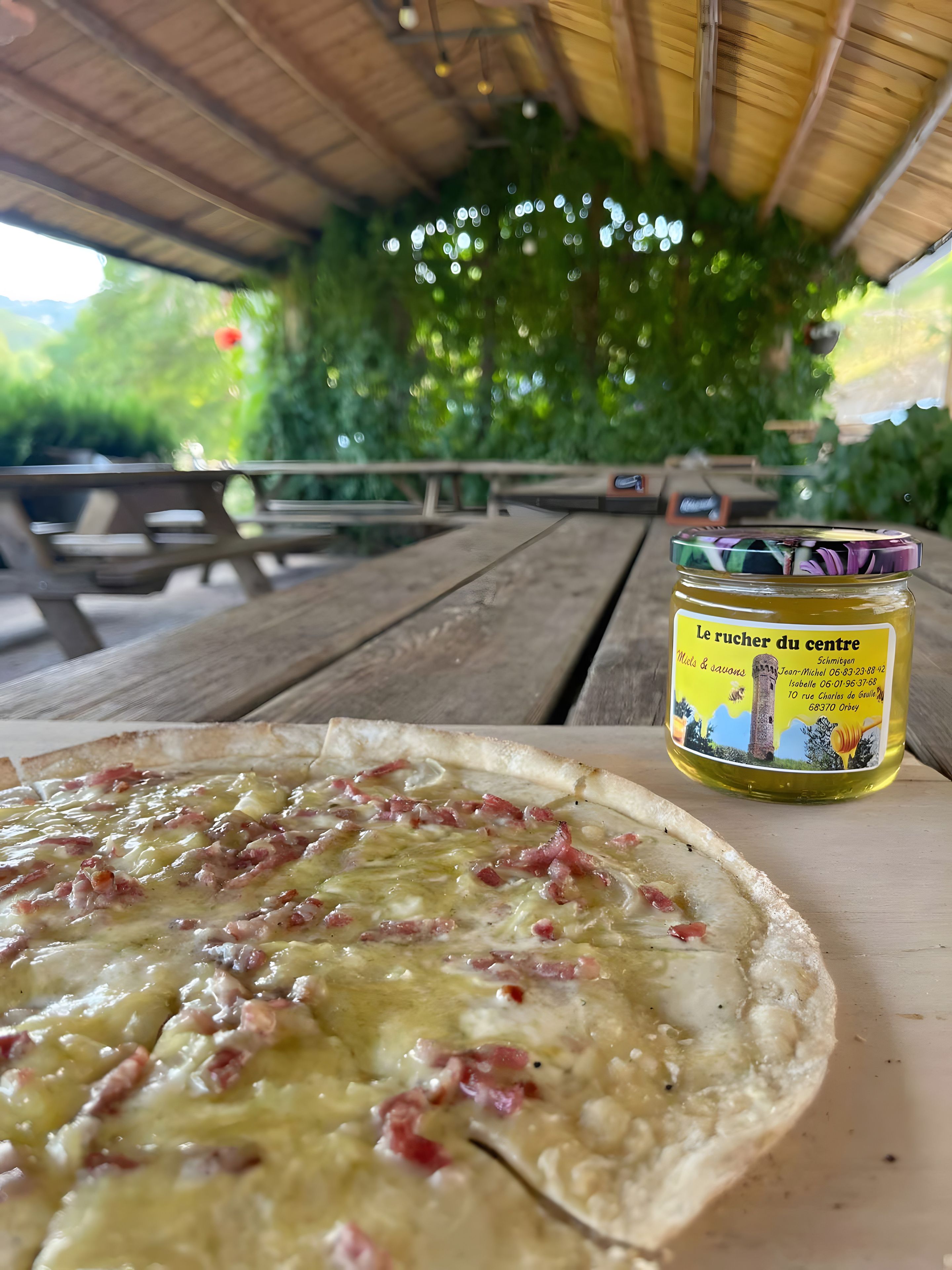 A pizza on a wooden table with a jar of honey mustard in the background.