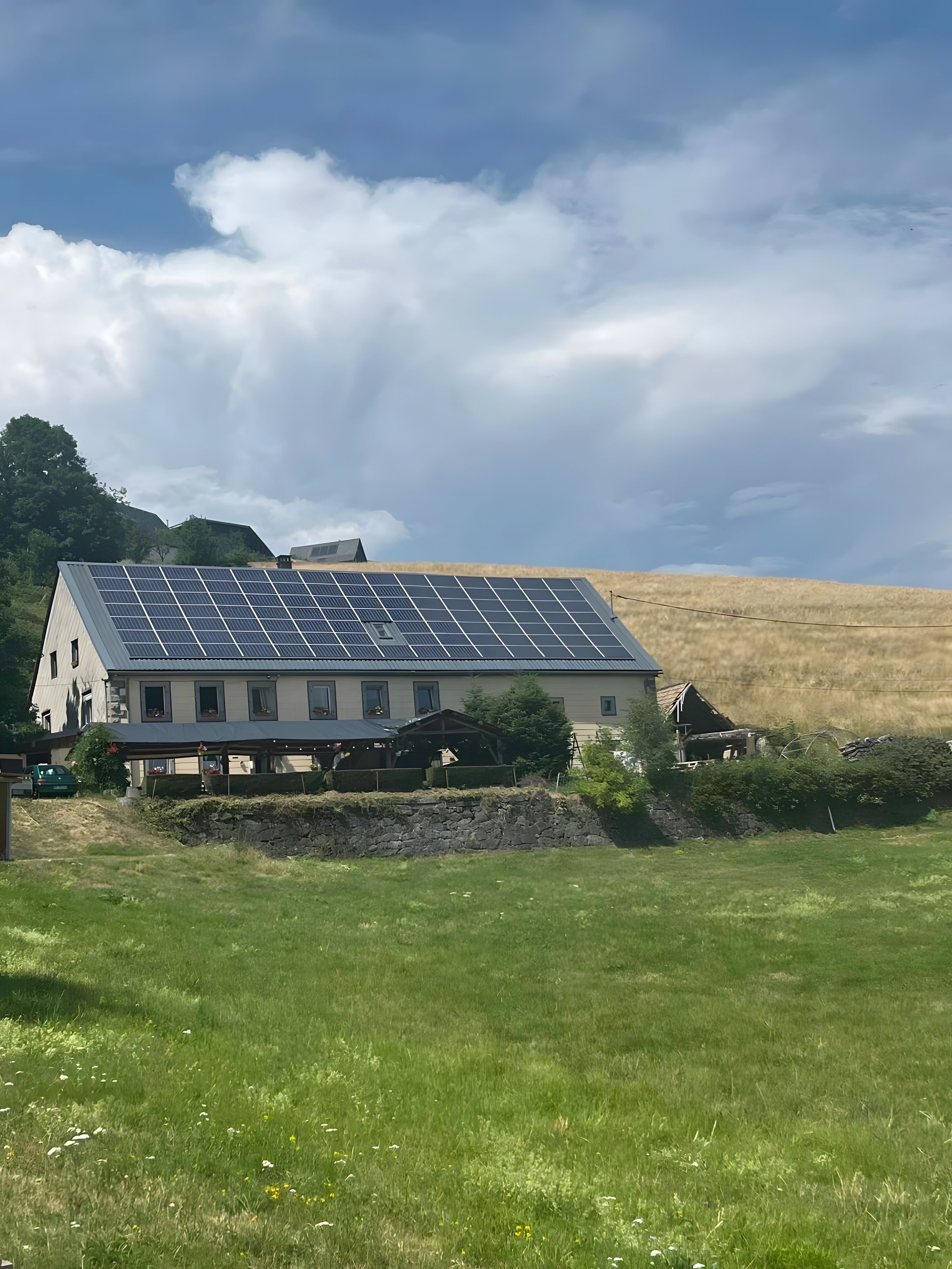 Une maison avec un toit recouvert de panneaux solaires et un mur de pierre à l’avant.