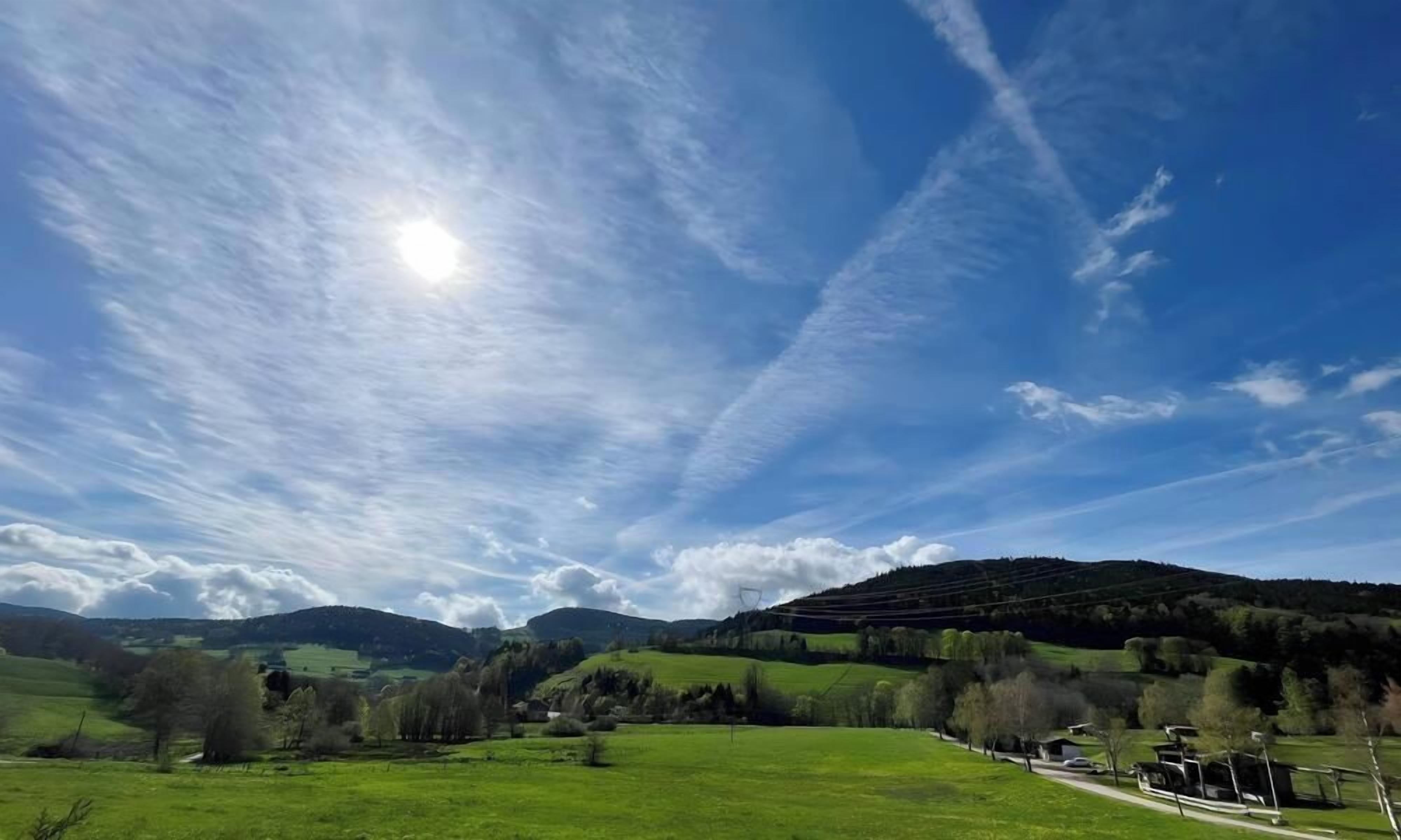 Un paysage rural avec des collines douces, un ciel dégagé et quelques bâtiments visibles au loin.