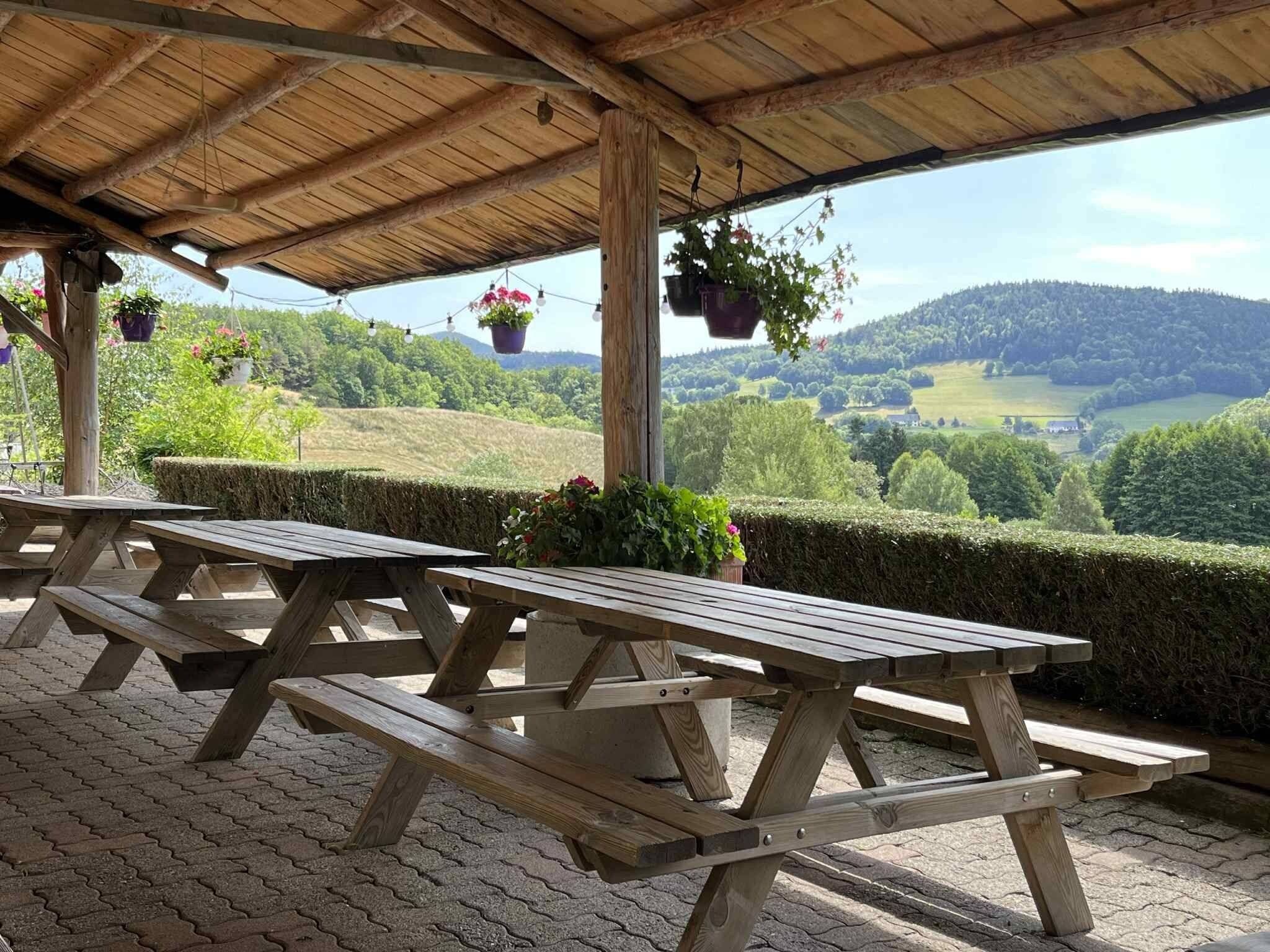 Un espace pique-nique abrité, doté de bancs en bois et de jardinières suspendues, offrant une vue sur une vallée verdoyante.