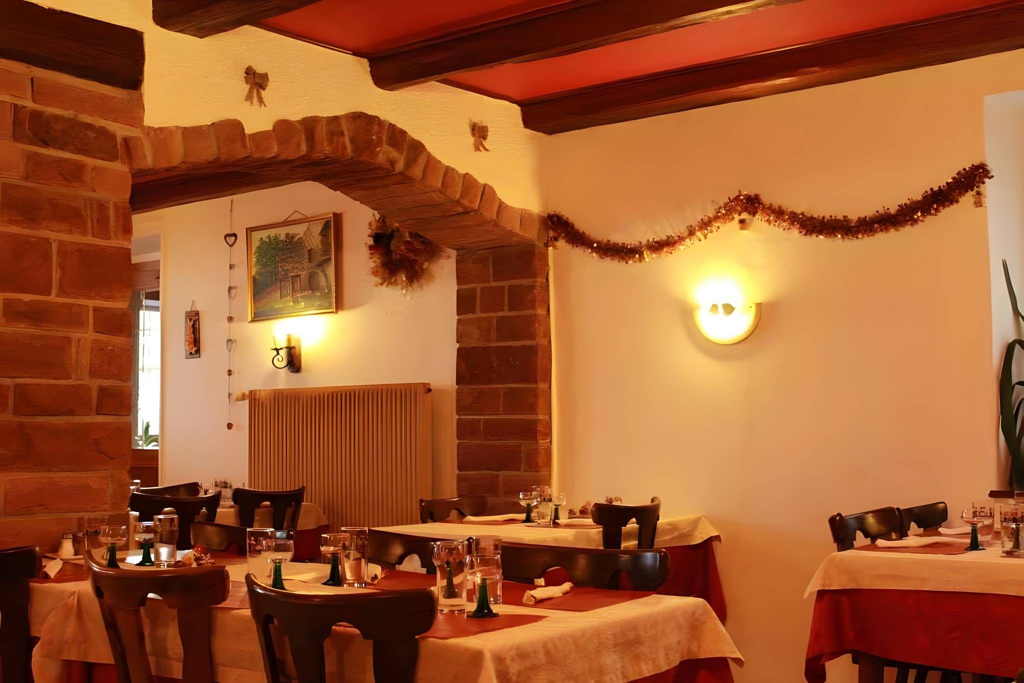 L’intérieur d’un restaurant avec des murs en briques, des poutres en bois et des tables dressées pour le service.