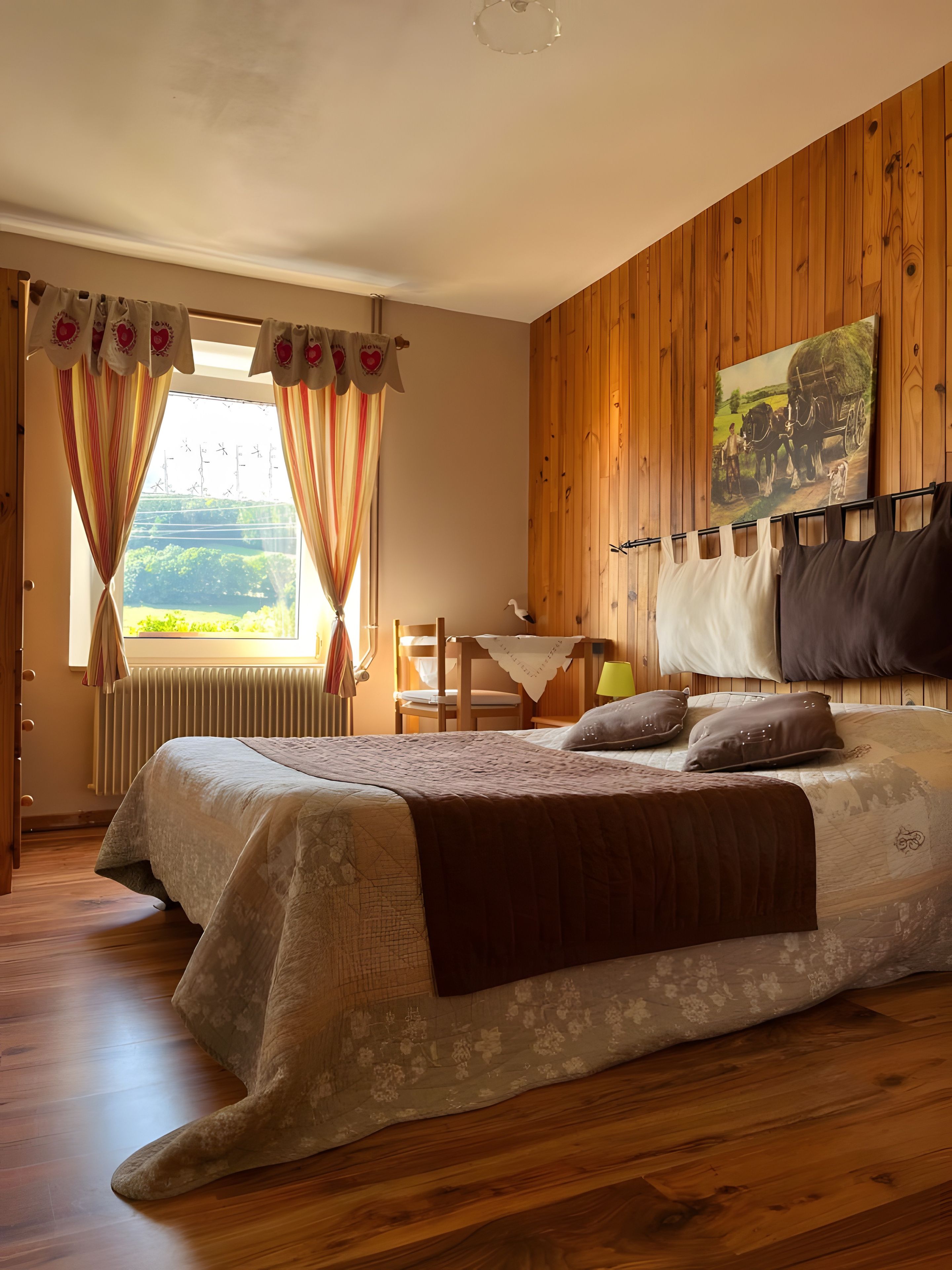 Une chambre avec un grand lit, des murs en bois, un tableau et une vue sur la verdure à l’extérieur.