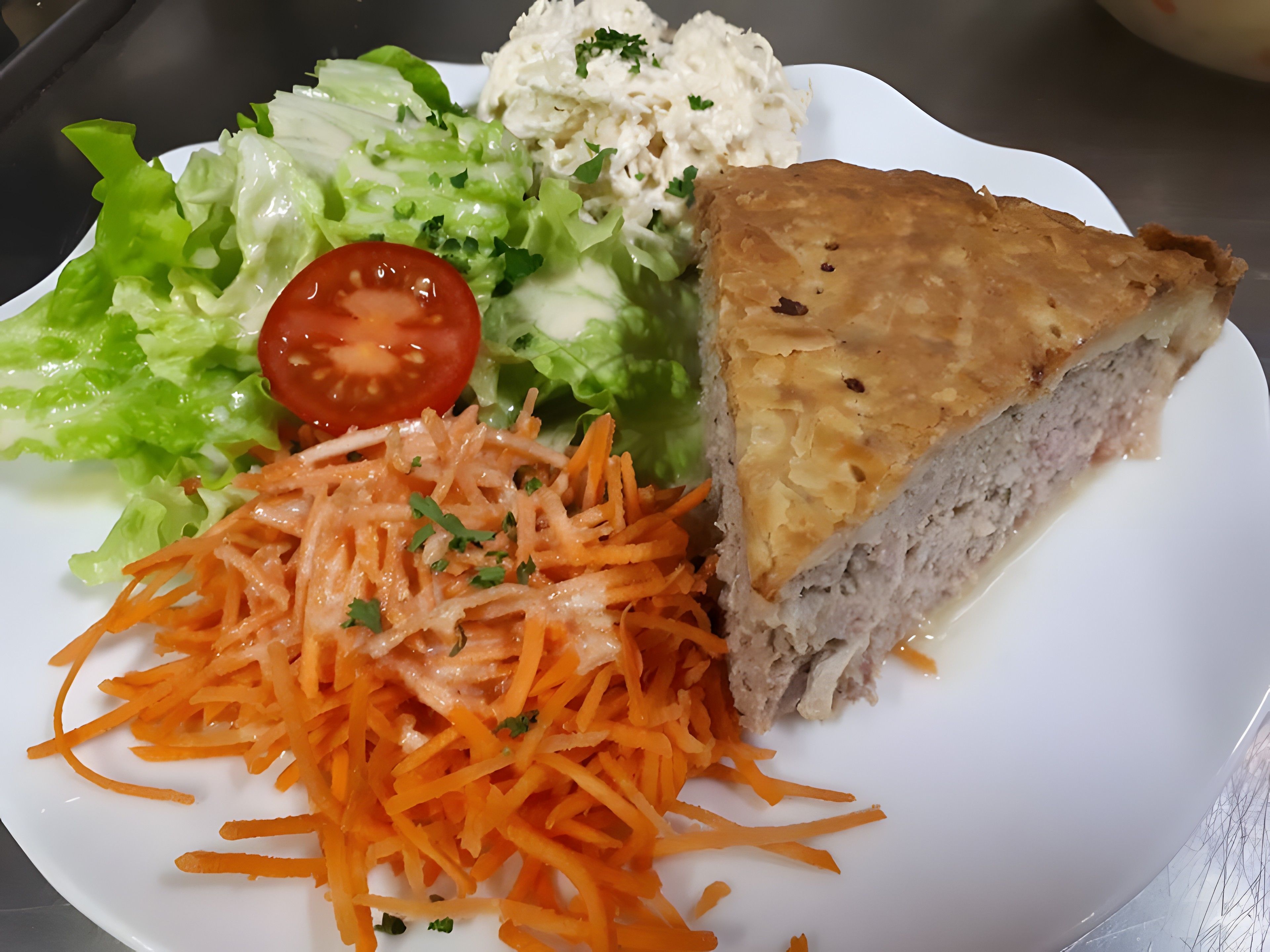 A plate with a slice of pie, a salad, and shredded carrots.