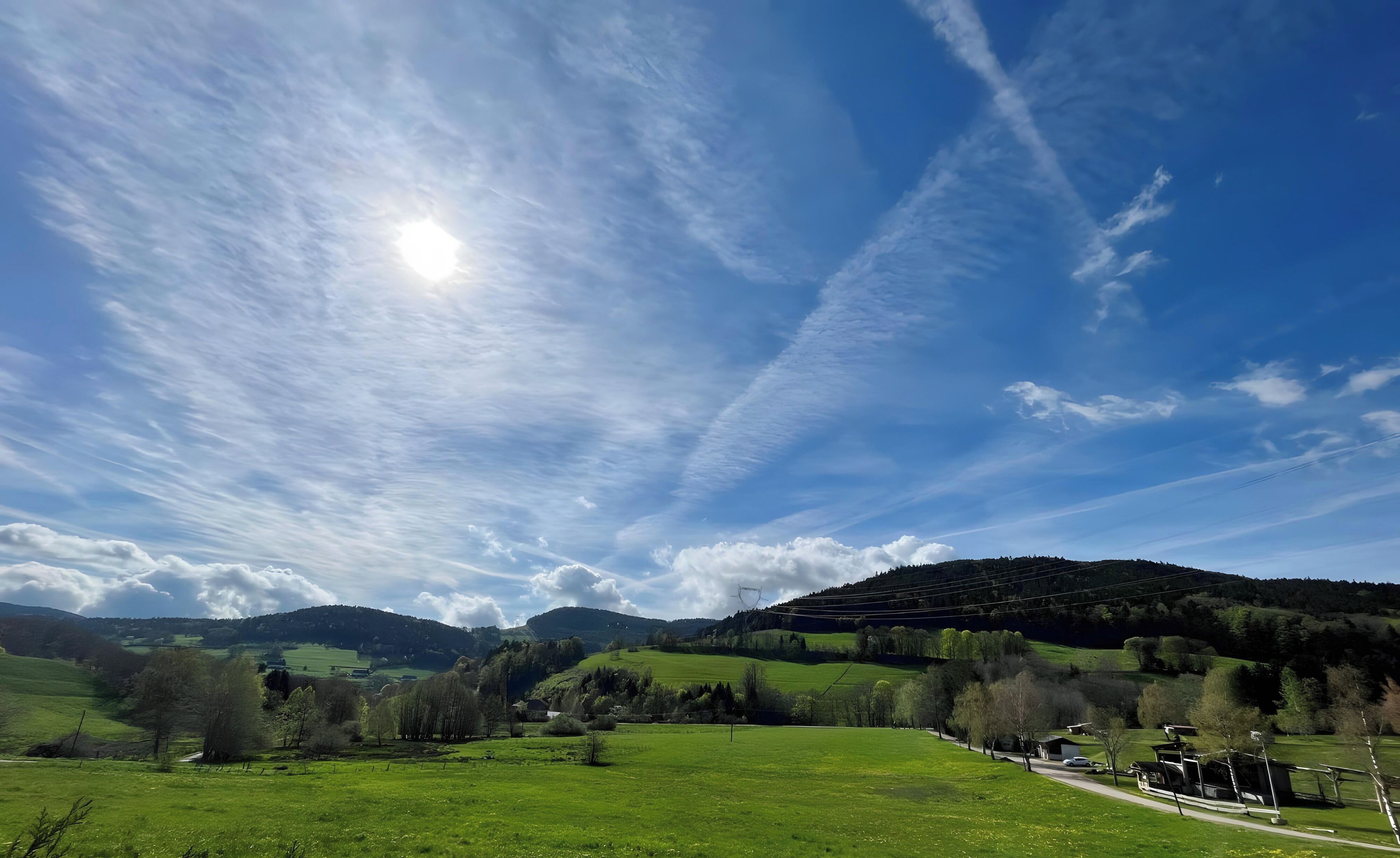 Un paysage rural caractérisé par un ciel dégagé, des champs verdoyants et une colline qui se dessine à l’horizon.