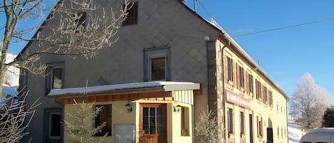 Un bâtiment à deux étages, avec un toit enneigé et un petit porche.