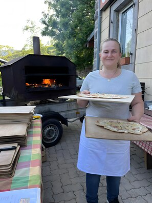 Une personne tenant une pizza sur une planche en bois, debout devant un four en briques.