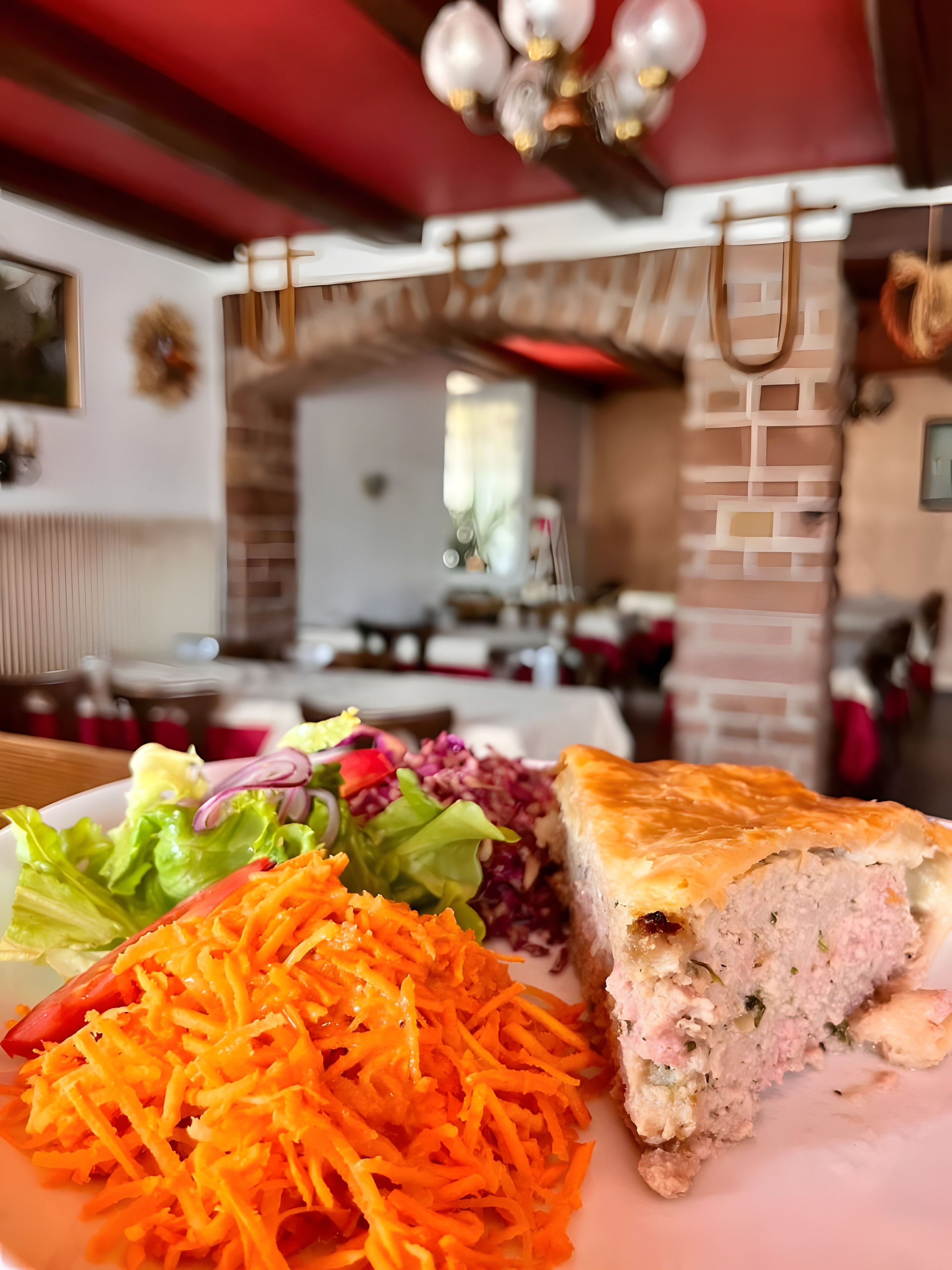 A plate with a slice of meat pie, shredded carrots, and a salad.