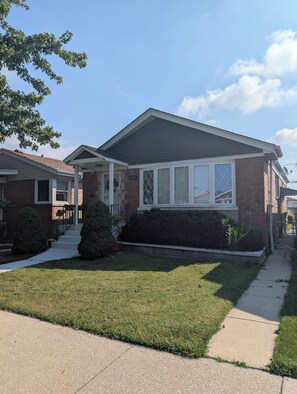 A two-story residential house with a brick facade, large windows, and a well-maintained lawn. - Comfortable 3BR getaway 5 min from Midway Airport and 15 min to Downtown. (Chicago)