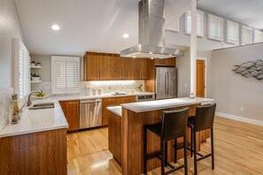 A modern kitchen with wooden cabinets, stainless steel appliances, and a bar area with stools. - Festival-Season Basecamp, Walk to Pearl St Theaters (Boulder)