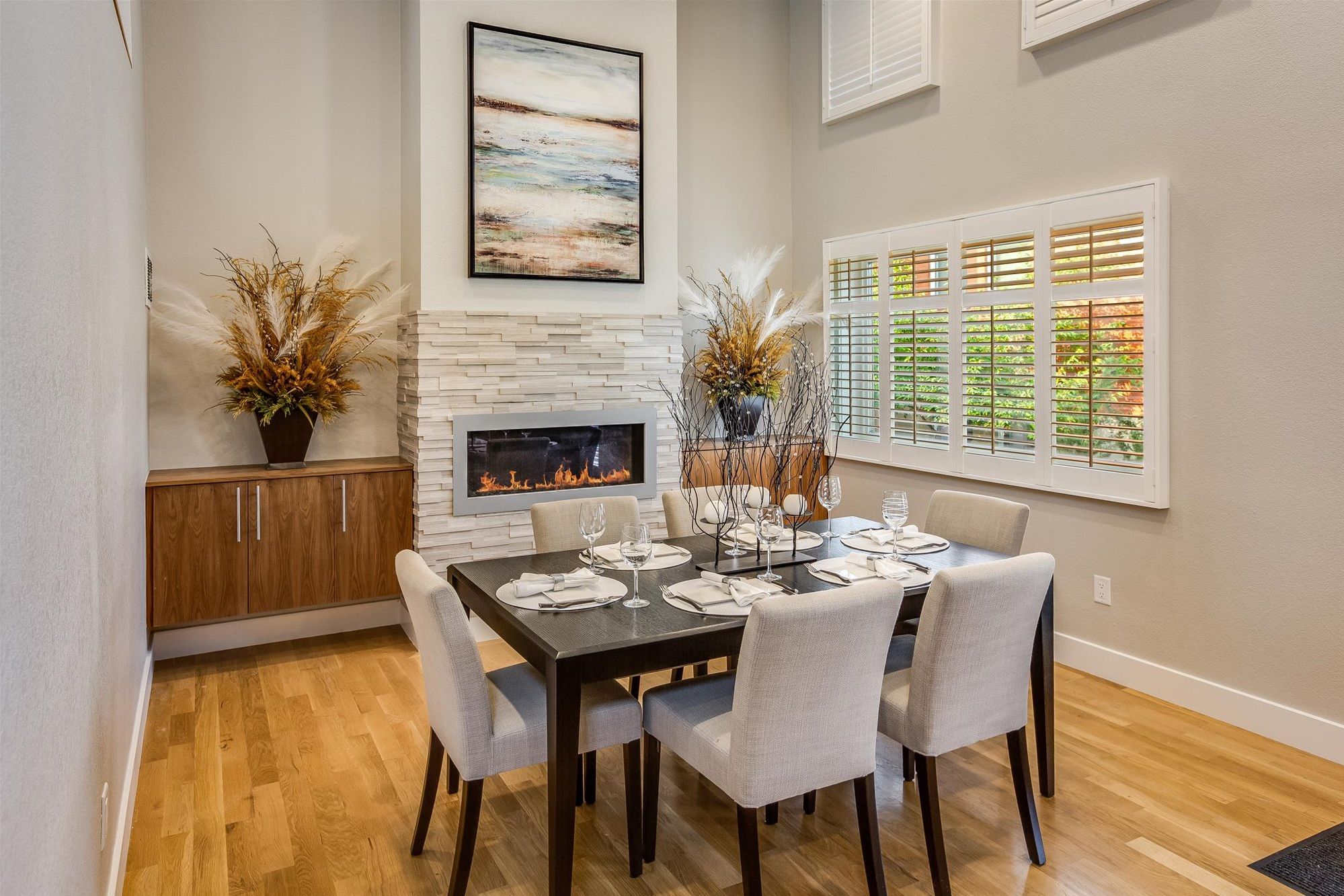 A dining area with a fireplace, a table set for six, and a window with blinds.
