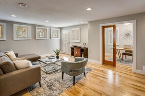 A spacious living room with a sofa, armchair, coffee table, and a dining area with a desk and chair. - Festival-Season Basecamp, Walk to Pearl St Theaters (Boulder)