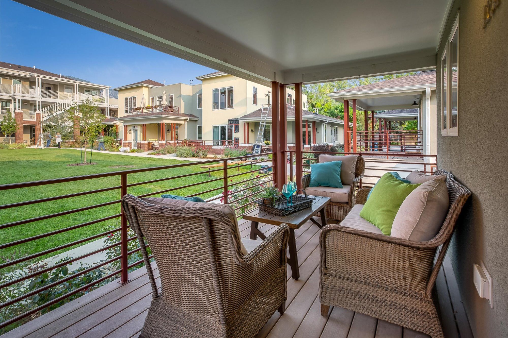 A covered balcony with wicker furniture, a small table, and a view of neighboring houses.