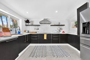 Cozinha moderna com armários pretos, exaustor de aço inoxidável e máquina de café embutida.