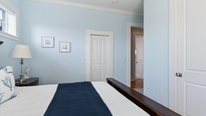 Quarto com cama, mesa de cabeceira, abajur e quadros nas paredes.