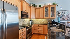A modern kitchen with wooden cabinets, stainless steel appliances, and a tiled backsplash. - 3rd Floor OceanView Condo Steps to Beach - Shared Pool & Putting Green - On-Site Parking (Bradenton Beach)