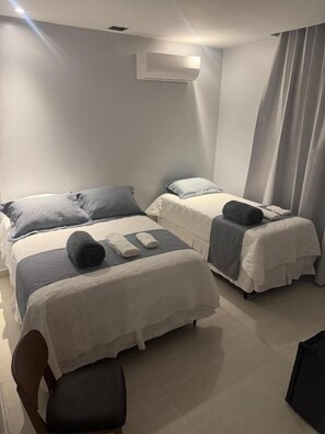 Habitación de hotel con dos camas, una silla, un escritorio y un ventanal con cortinas.