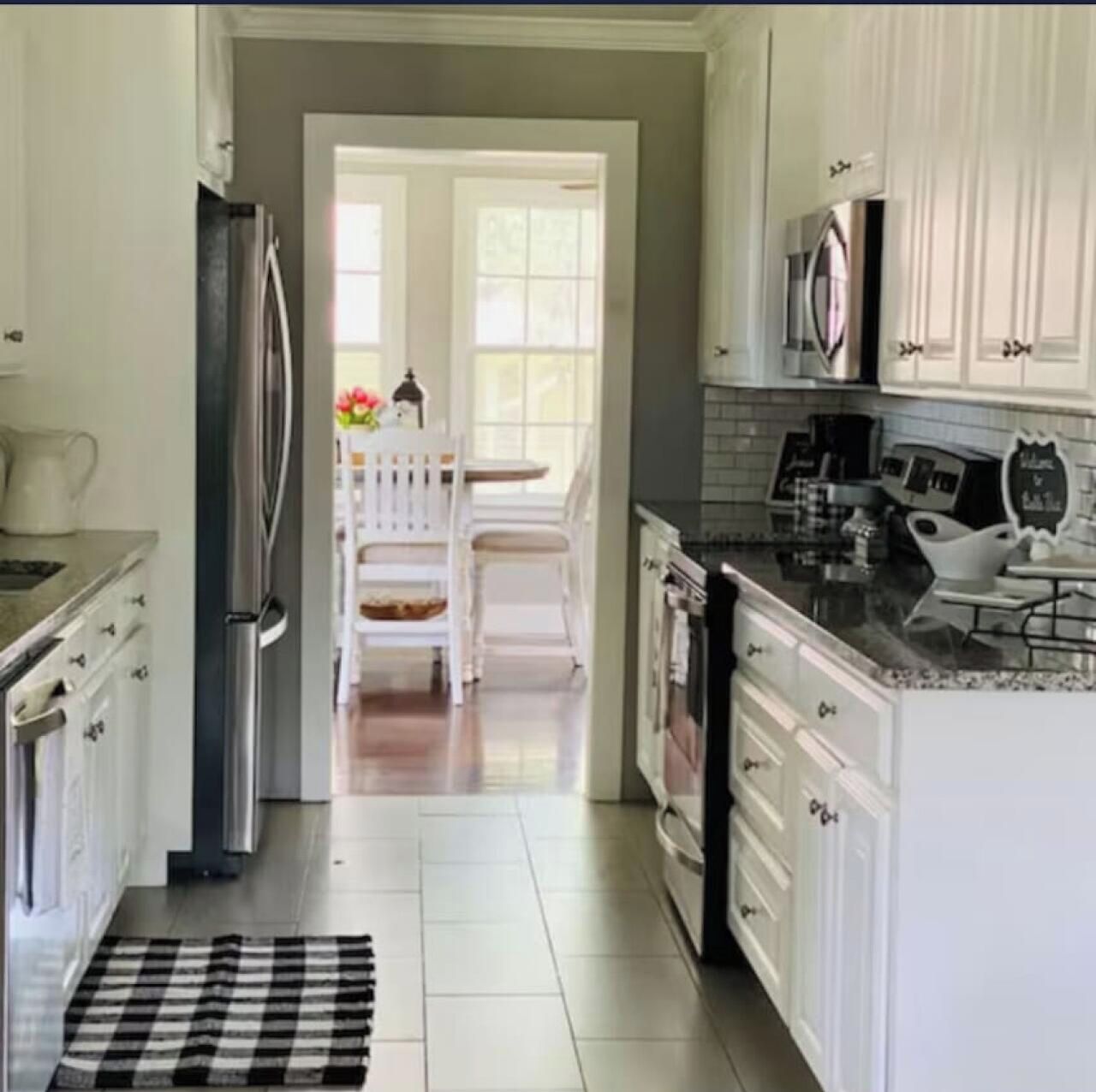 A kitchen with white cabinets, a refrigerator, a coffee maker, and a dining area with a white table and chairs.