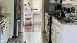 A kitchen with white cabinets, a refrigerator, a coffee maker, and a dining area with a white table and chairs.