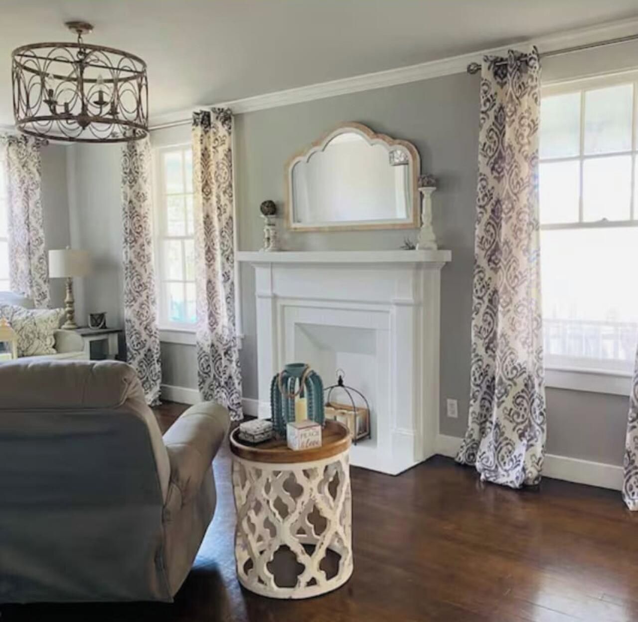 A room with a fireplace, a chandelier, patterned curtains, and a side table with decorative items.