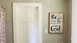 A bathroom with a white door, a toilet, a basket of towels, and a motivational quote on the wall.