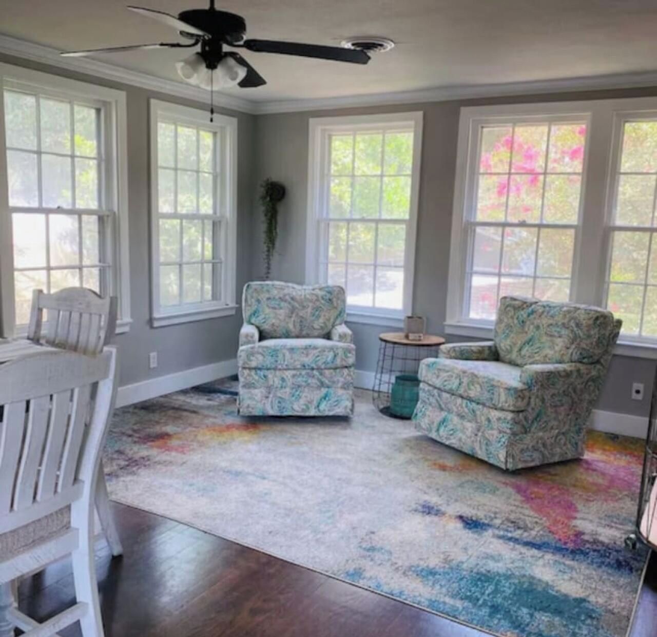 A room with a ceiling fan, two armchairs, a small table, and a colorful rug.