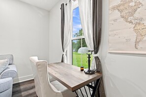 Ein Eckzimmer mit einem Holztisch, einem weißen Stuhl, einer Lampe und einer Karte an der Wand.