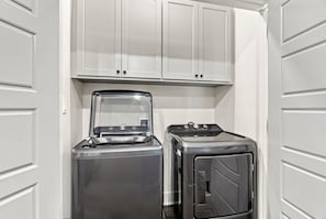 Ein kleiner Hauswirtschaftsraum mit Waschmaschine und Trockner, weißen Schränken darüber und einer Tür links.