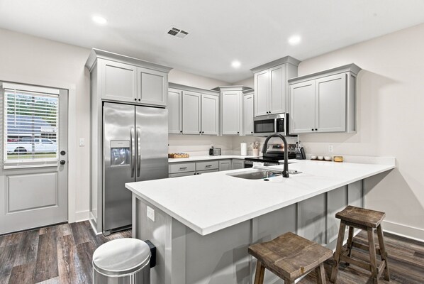 A modern kitchen with white cabinetry, stainless steel appliances, a large island with a sink, and a window with blinds.