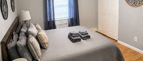 A bedroom with a bed, pillows, a bedside lamp, a window with curtains, and a door.