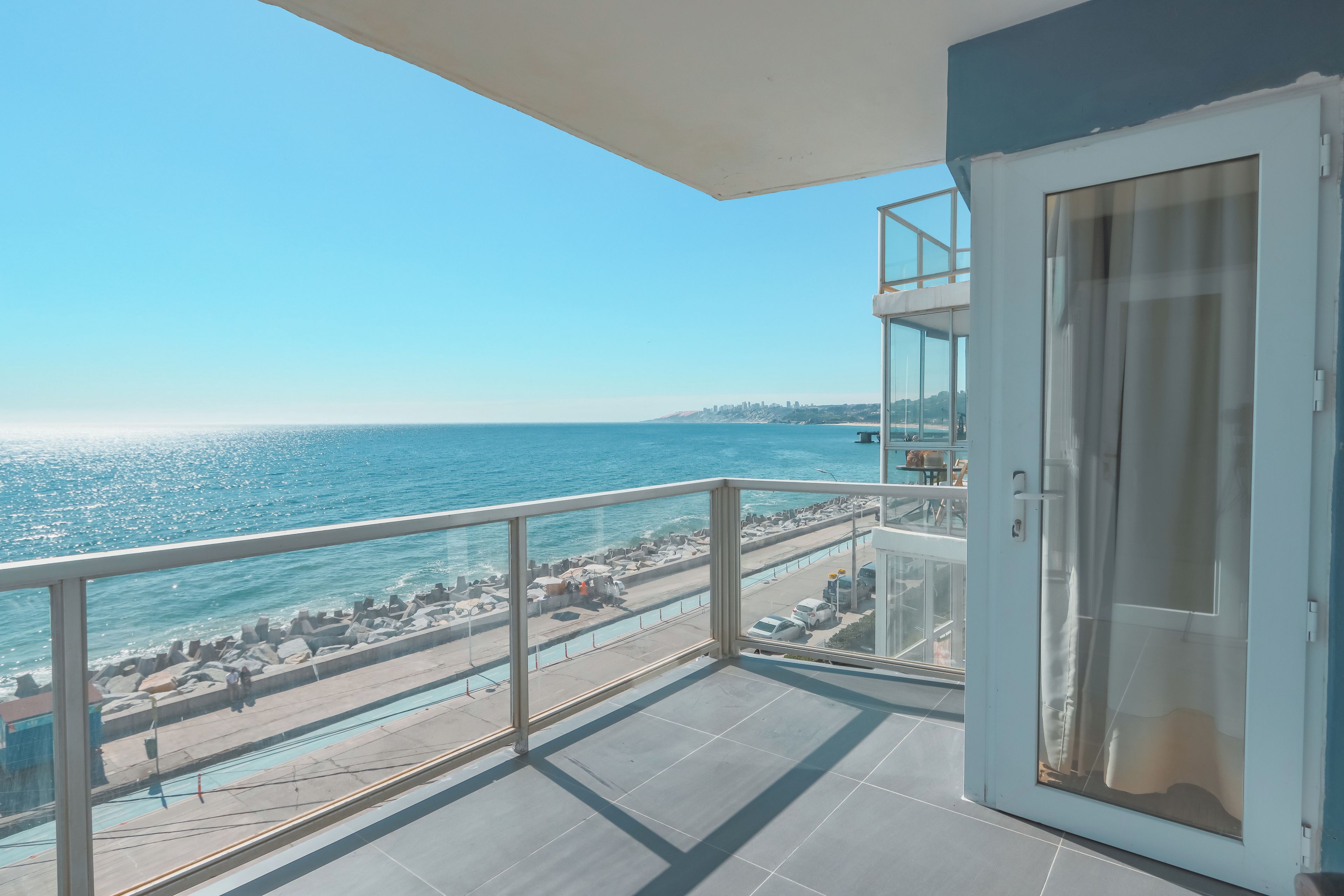 A balcony with a clear view of the sea and a distant cityscape.
