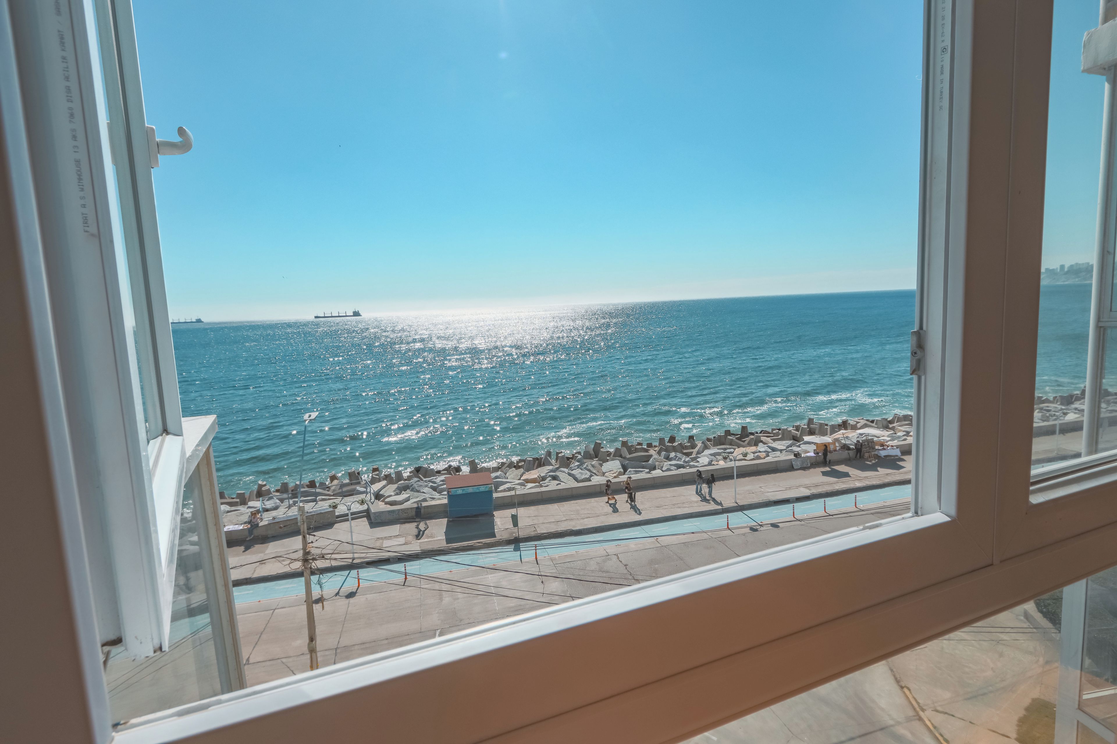 Une vue d’une promenade en bord de mer, avec un ciel dégagé, une étendue d’eau et un navire au loin.
