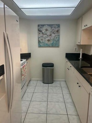Una cucina compatta con frigorifero, cestino e un quadro appeso al muro.