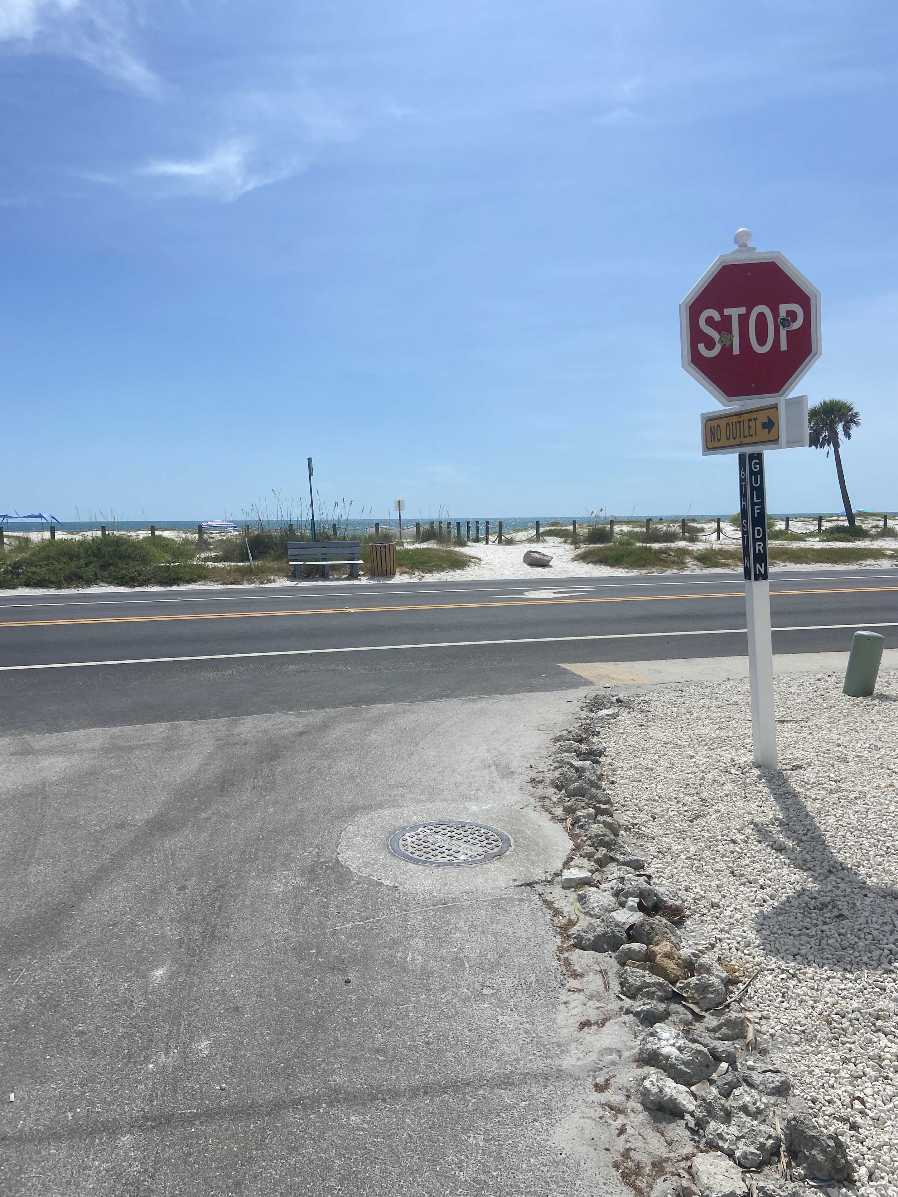 Un panneau de signalisation indiquant l’obligation de s’arrêter, placé à une intersection près d’une plage, sous un ciel dégagé.
