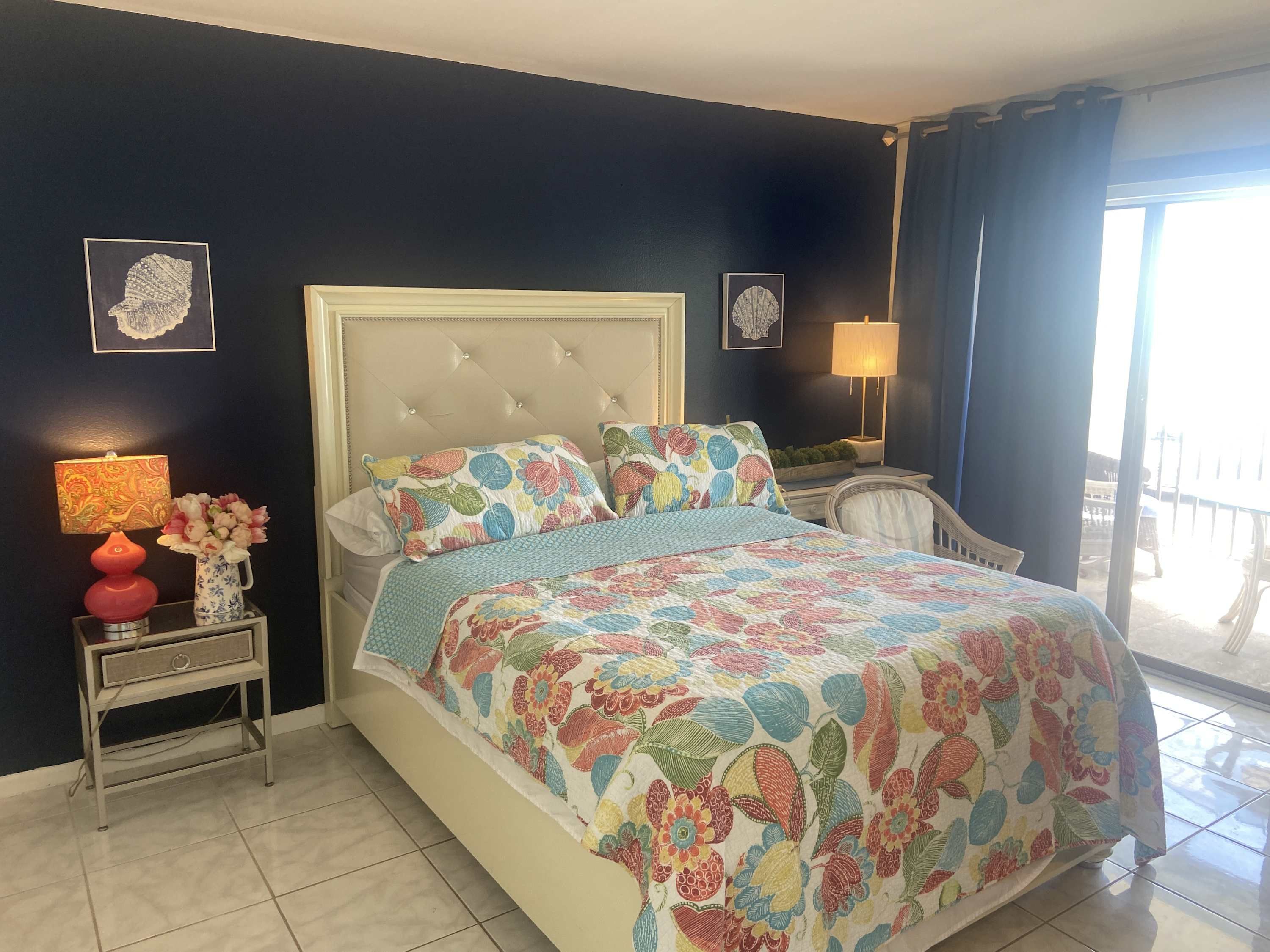 Ein Schlafzimmer mit einem Bett, einem Nachttisch mit Lampe, einer Blumenvase und einem Sessel.