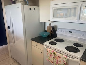 A kitchen with a white refrigerator, a microwave, and a stove with a floral towel. - Ocean View! Come Escape with Us! (Bradenton Beach)
