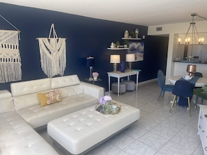 A modern living room with a white sofa, a coffee table, and a dining area with chairs and a table. - Ocean View! Come Escape with Us! (Bradenton Beach)