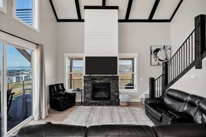 A spacious living room with a fireplace, black leather sofas, and a large TV. - Lakeview Gamehouse | Ideal Beach Access+EV Charger (Garden City)