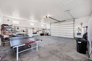 A spacious indoor area with a ping pong table, storage cabinets, and a garage door. - Lakeview Gamehouse | Ideal Beach Access+EV Charger (Garden City)