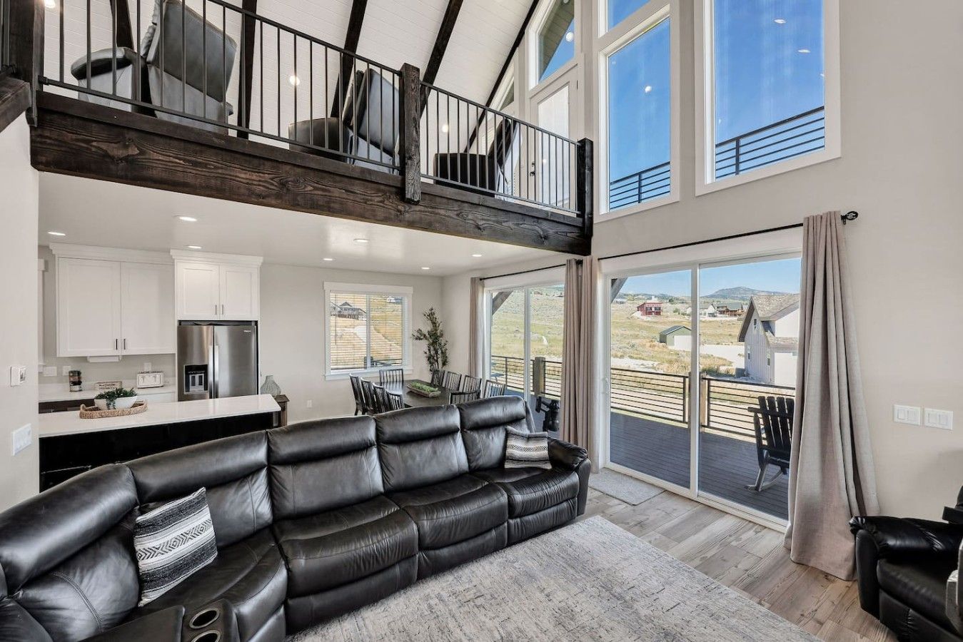 A spacious living area with a black leather sofa, a dining table, and a kitchen in the background.