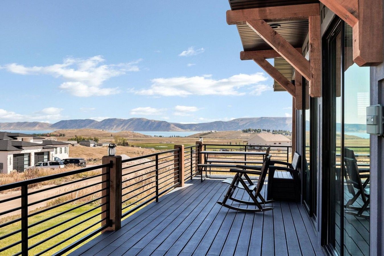 A deck with a view of mountains and a lake, wooden railings, and a rocking chair.