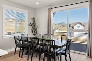 Uma área de refeições com mesa e cadeiras, janelas amplas e vista para casas.