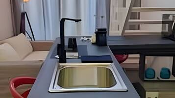 A compact kitchen with a sink, countertop, and a small table with a coffee maker.