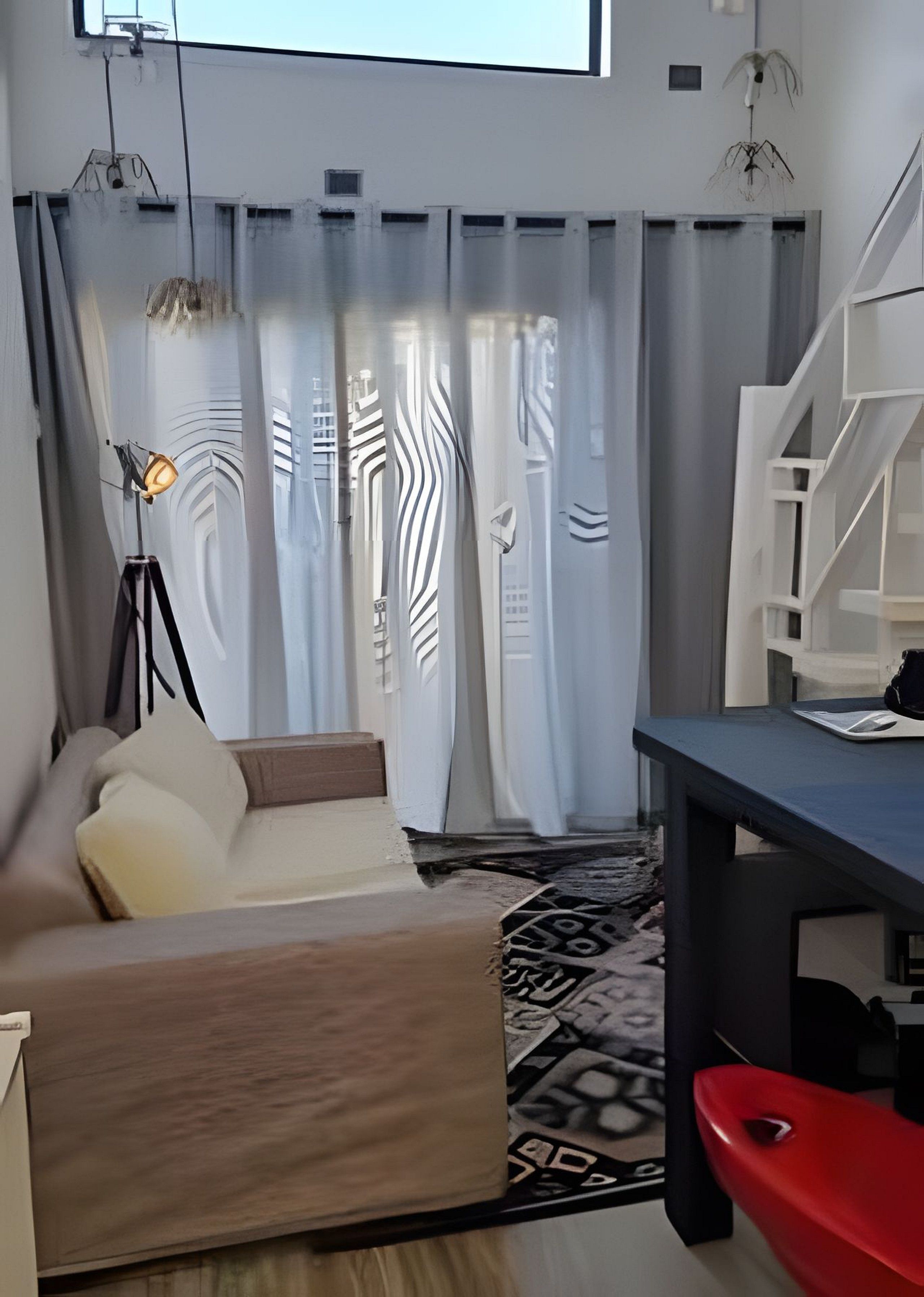 Una sala de estar moderna con un sofá, una mesa de comedor y una silla roja. Hay una lámpara de pie y cortinas con un diseño geométrico.