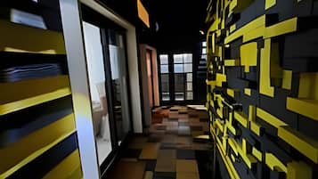 Un pasillo con piso de patrón de cuadros, una entrada con puerta de vidrio y una pared con diseños geométricos amarillos y negros.