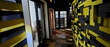 A corridor with a checkered floor pattern, a glass door entrance, and a wall with geometric yellow and black patterns.