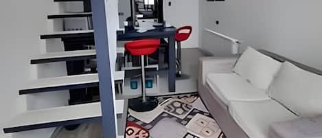 Un interior moderno con una escalera que lleva a una zona de altillo, una mesa de comedor con sillas y un sofá.