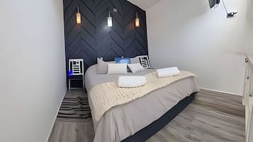 Un dormitorio moderno con cabecera de diseño en patrón espiga, cama con cubrecama color beige y lámparas de noche.