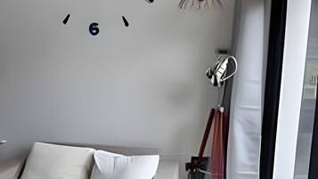 Ein modernes Wohnzimmer mit einer Couch, einer Wanduhr und einem großen Fenster.