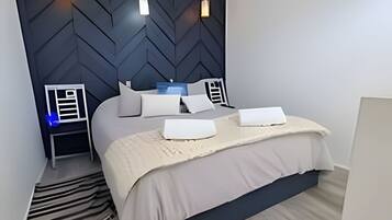 A modern bedroom with a herringbone-patterned headboard, a bed with white linens, and a nightstand with a lamp.